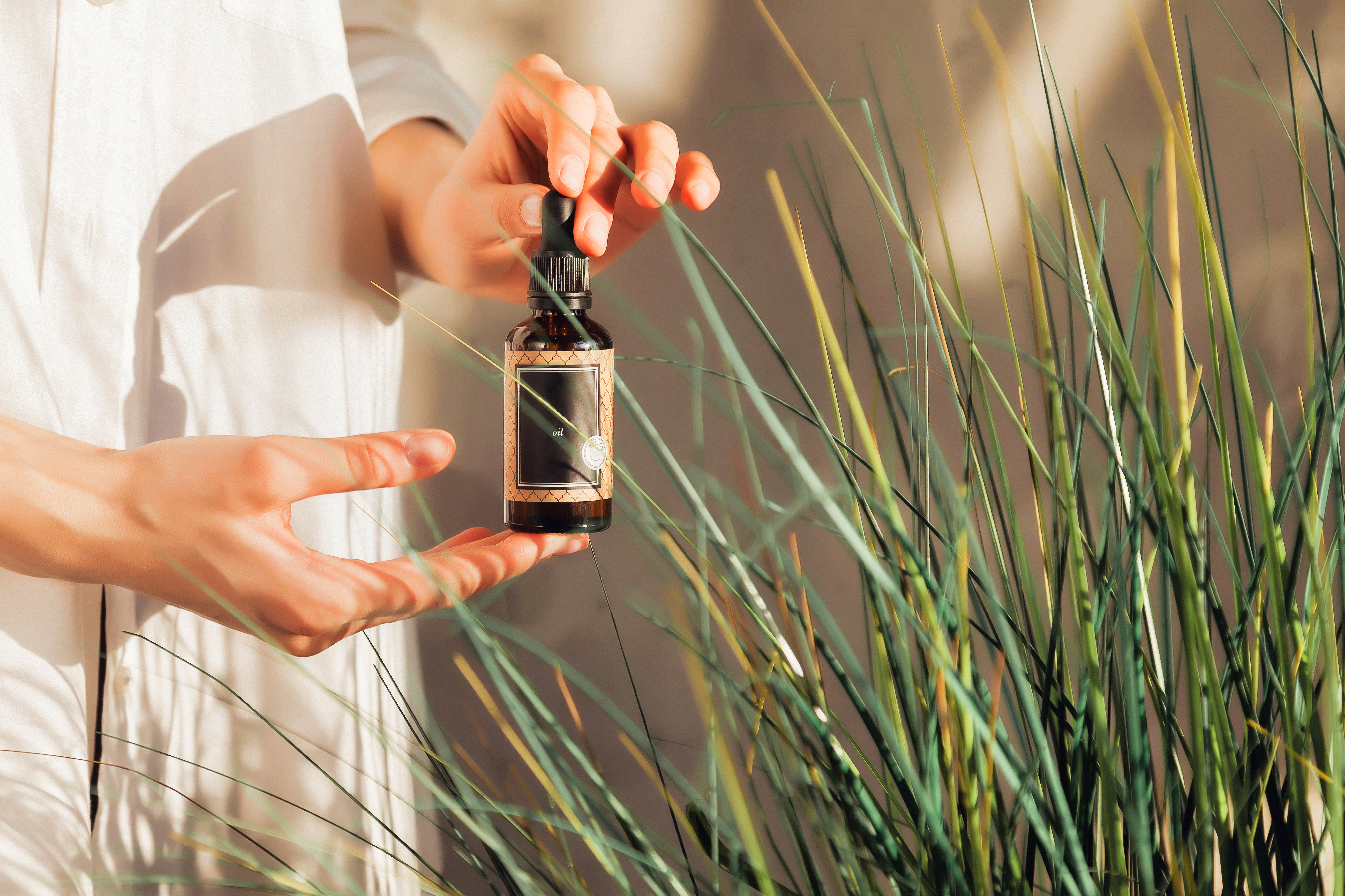 Woman hands holding massage or cosmetics oil bottles. Close up essential oil on chair. High angle view of massage oil bottle on leaf background. Concept of healthy lifestyle and self care. Copy space