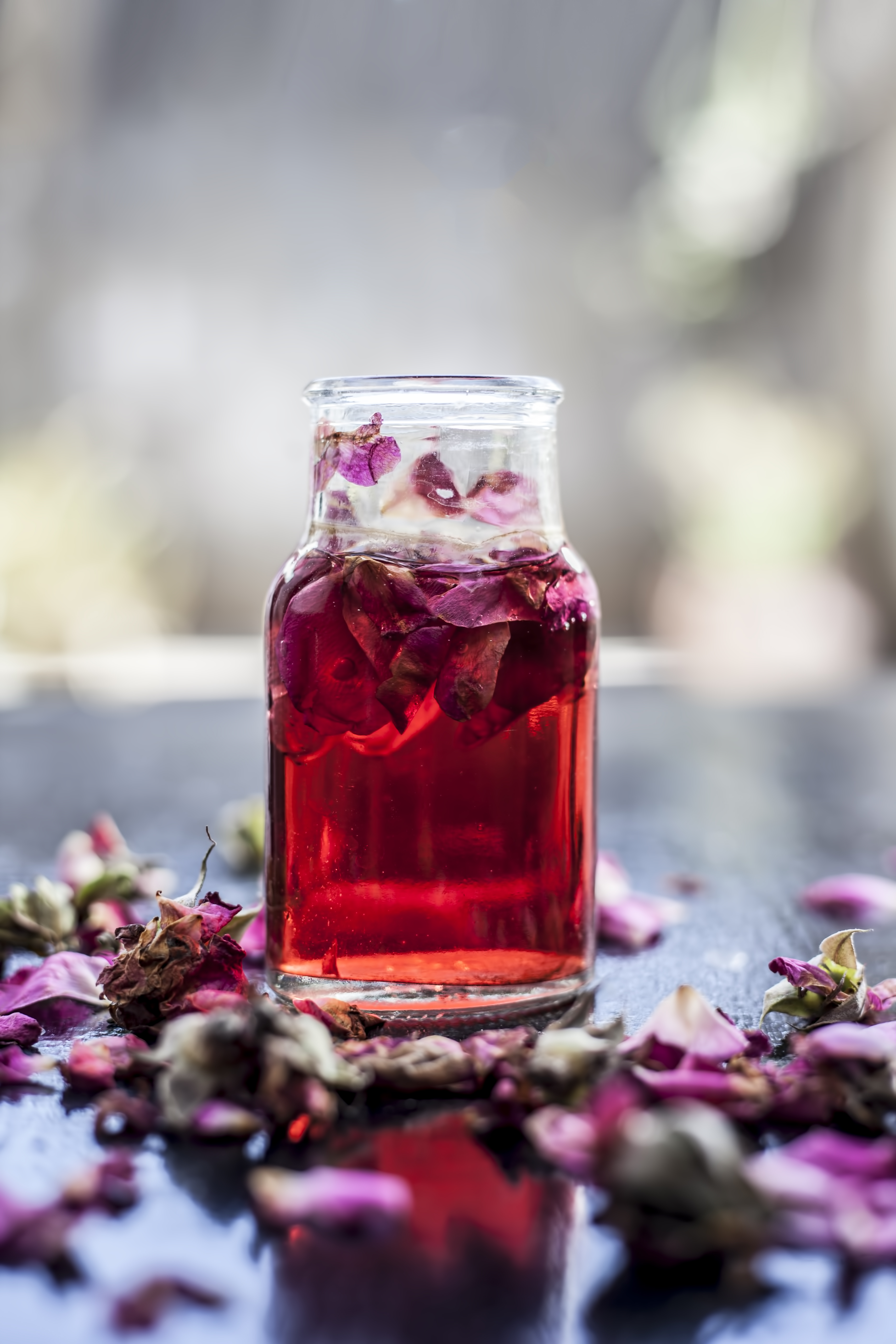Rose water or Gulab jal or Gulab ka pani or Rosa water in a bottle on wooden surface with rose petals.